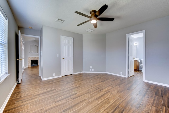 unfurnished bedroom with visible vents, a textured ceiling, wood finished floors, a fireplace, and baseboards