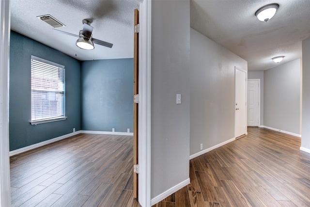 unfurnished room featuring a ceiling fan, wood finished floors, visible vents, and a textured ceiling