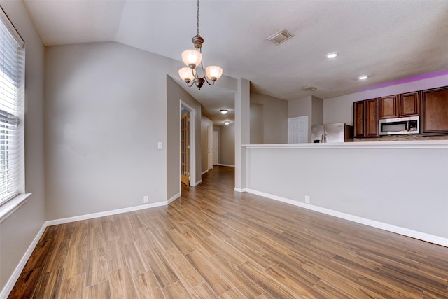 unfurnished living room with a chandelier, visible vents, light wood-style flooring, and plenty of natural light