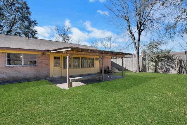 back of house with fence, a yard, a shingled roof, brick siding, and a patio area