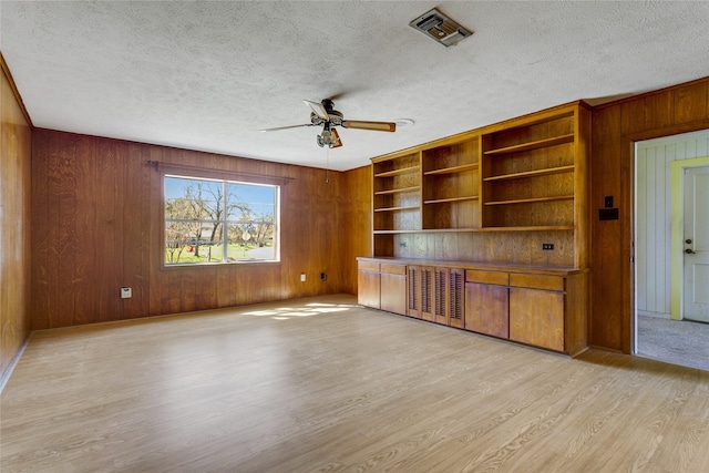 unfurnished living room with visible vents, light wood-style floors, wood walls, and a textured ceiling