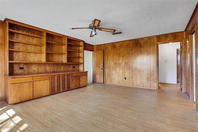 unfurnished living room featuring visible vents, a textured ceiling, wooden walls, light wood finished floors, and ceiling fan