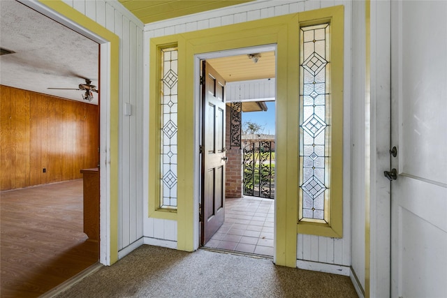 carpeted foyer featuring a ceiling fan and wood walls