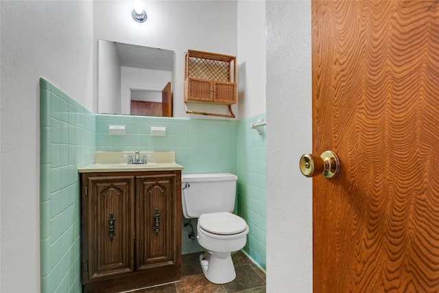 half bath featuring a wainscoted wall, vanity, toilet, and tile walls