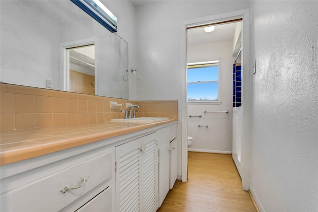 bathroom with toilet, backsplash, wood finished floors, baseboards, and vanity