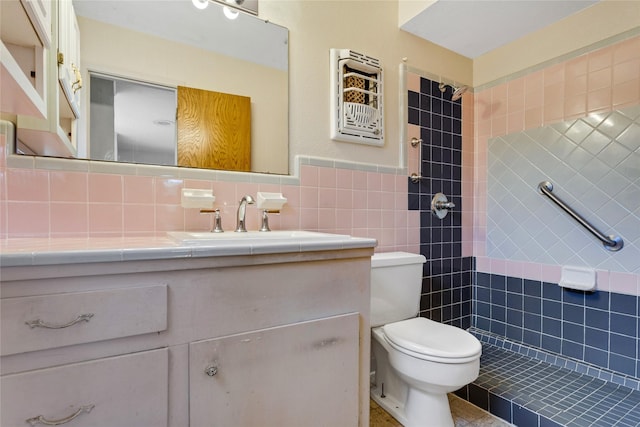 bathroom with vanity, tile walls, toilet, and tiled shower