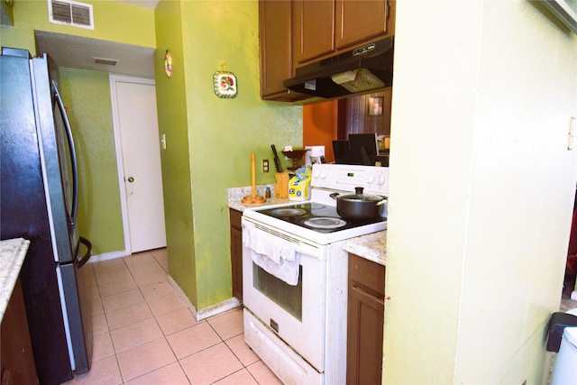 kitchen with visible vents, under cabinet range hood, light tile patterned floors, freestanding refrigerator, and electric stove