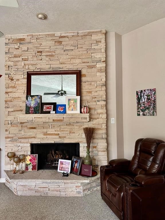 carpeted living room featuring a textured ceiling, a stone fireplace, and a ceiling fan