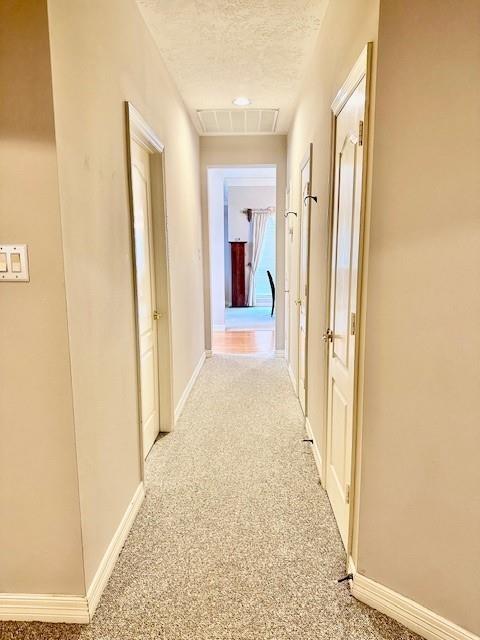 hallway featuring visible vents, light colored carpet, a textured ceiling, and baseboards