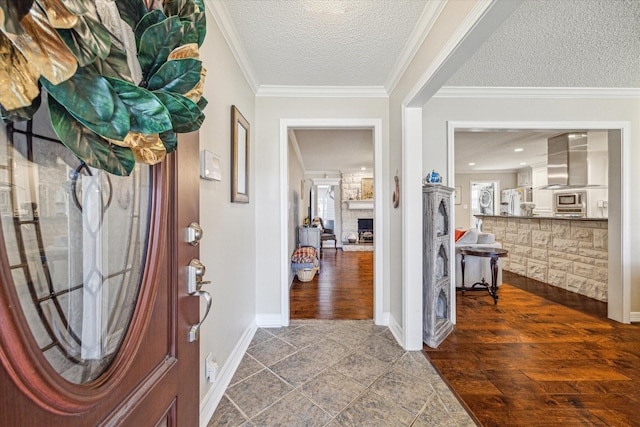 foyer entrance featuring a textured ceiling, dark wood-style floors, a stone fireplace, crown molding, and baseboards