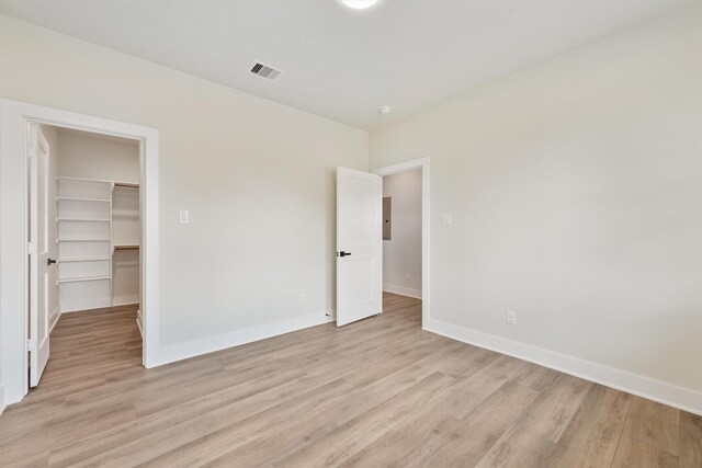 unfurnished bedroom with visible vents, baseboards, a walk in closet, and light wood-style floors