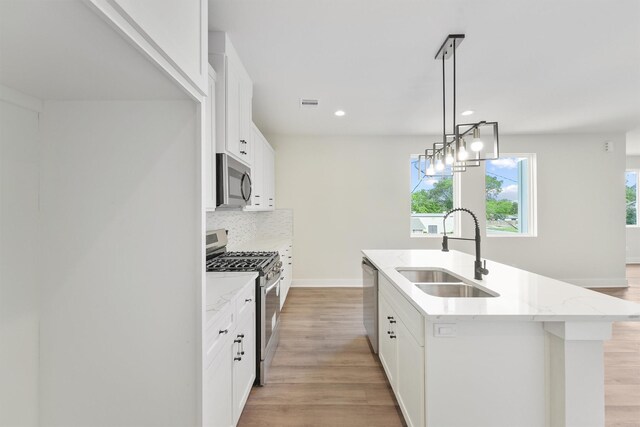 kitchen with a kitchen island with sink, a sink, backsplash, stainless steel appliances, and light wood-style floors