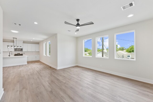 unfurnished living room with light wood-type flooring, visible vents, and a healthy amount of sunlight