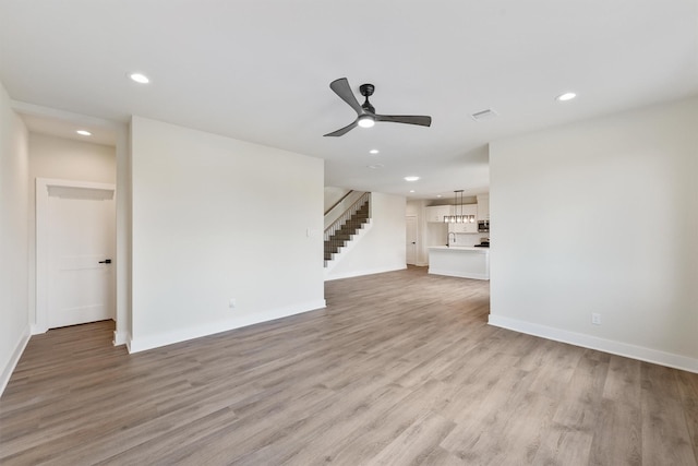 unfurnished living room featuring recessed lighting, light wood finished floors, baseboards, ceiling fan, and stairs