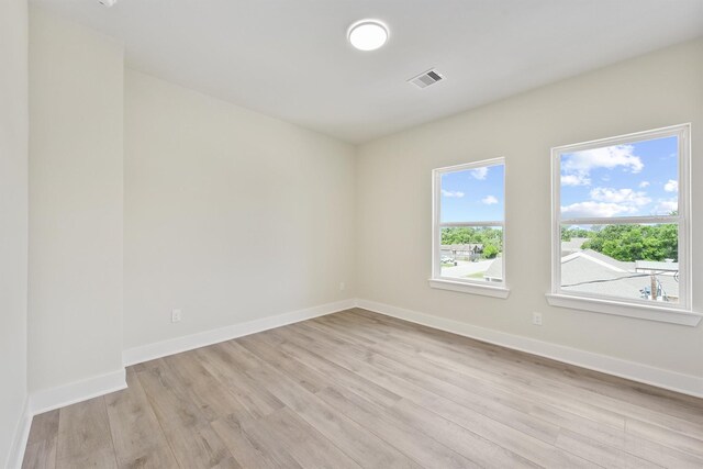 unfurnished room featuring light wood finished floors, visible vents, and baseboards