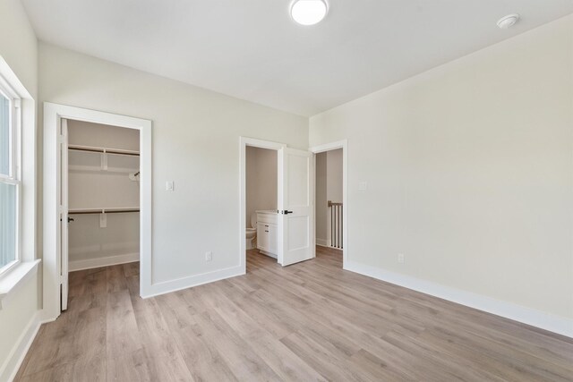 unfurnished bedroom featuring a walk in closet, baseboards, and light wood-style floors