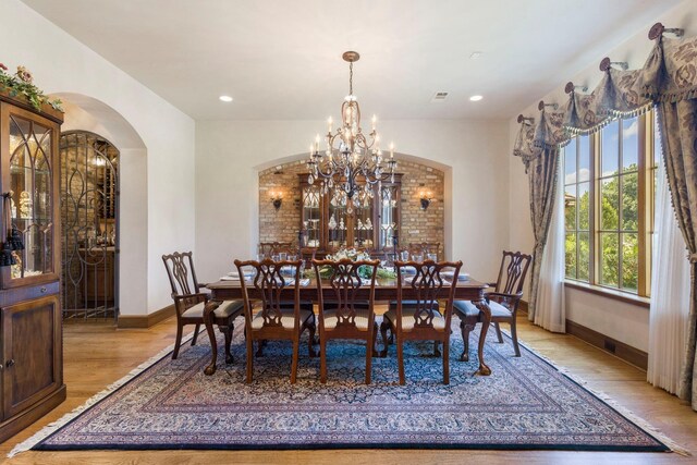 dining room featuring baseboards, light wood-type flooring, recessed lighting, arched walkways, and a notable chandelier