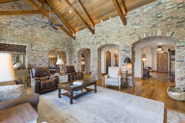 living room featuring ceiling fan, beamed ceiling, wood finished floors, arched walkways, and high vaulted ceiling