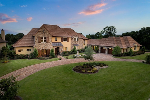 french country home with stucco siding, a front lawn, a garage, stone siding, and decorative driveway