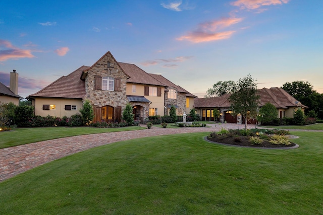 french country inspired facade with stone siding, stucco siding, decorative driveway, and a front yard