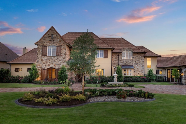 french country inspired facade featuring stucco siding and a yard