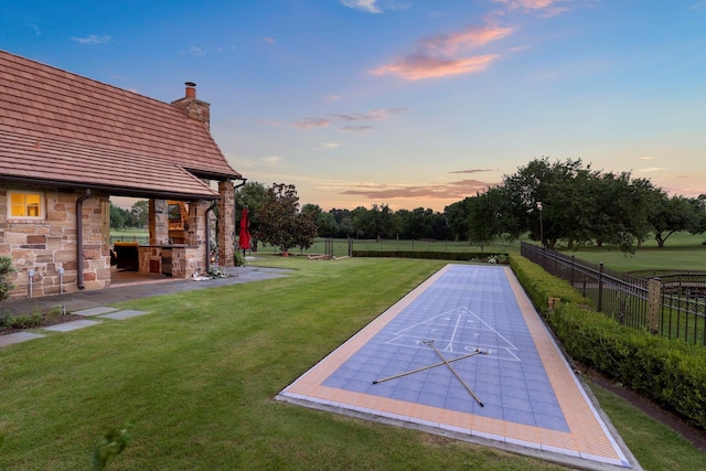 view of yard with shuffleboard, fence, and exterior fireplace