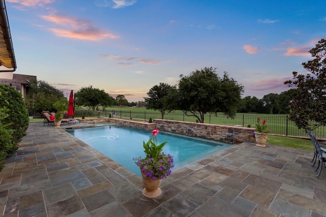 pool at dusk with a patio, a fenced backyard, and a fenced in pool