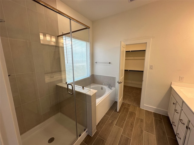 bathroom featuring wood finish floors, a walk in closet, a garden tub, a shower stall, and vanity