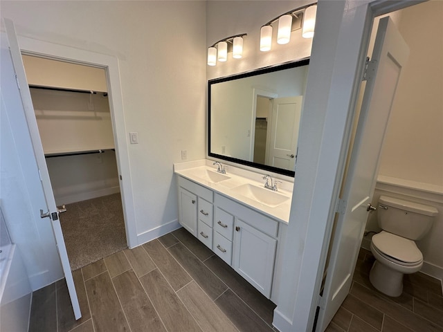 bathroom featuring a sink, a walk in closet, wood finish floors, and toilet