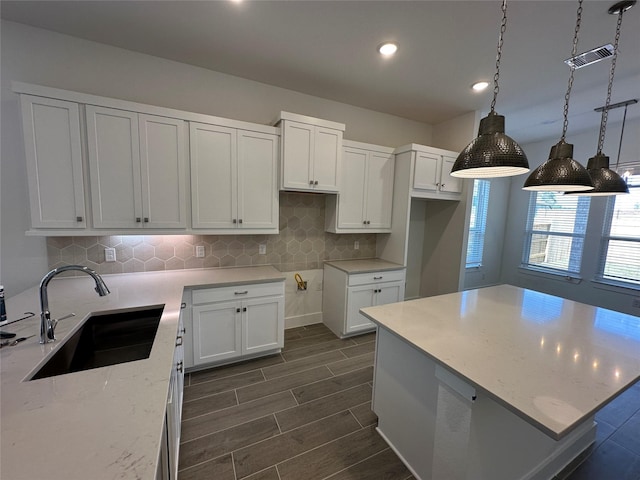 kitchen with light stone counters, visible vents, wood tiled floor, a sink, and white cabinetry