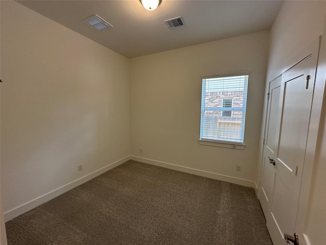 spare room featuring baseboards, visible vents, and dark colored carpet