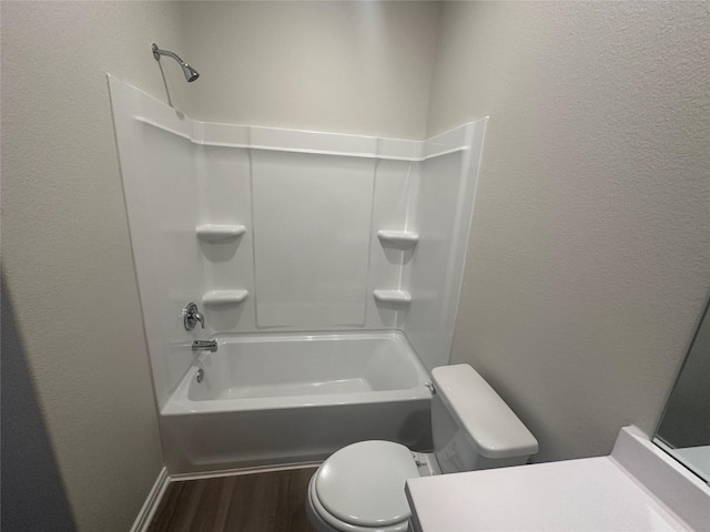 bathroom featuring toilet, wood finished floors, washtub / shower combination, vanity, and a textured wall