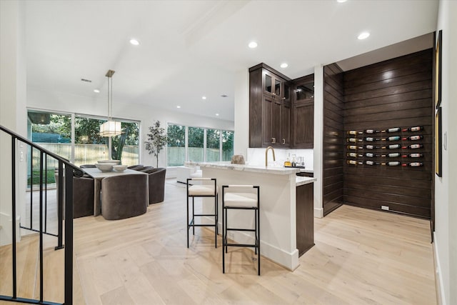 kitchen with dark brown cabinetry, light wood-style floors, glass insert cabinets, a kitchen breakfast bar, and open floor plan