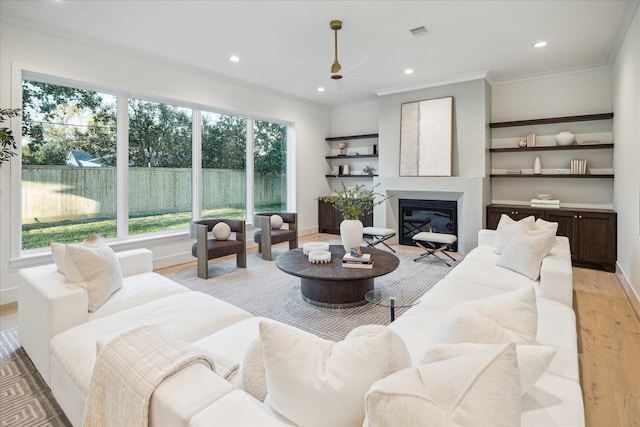 living area featuring light wood-type flooring, a ceiling fan, a glass covered fireplace, recessed lighting, and crown molding