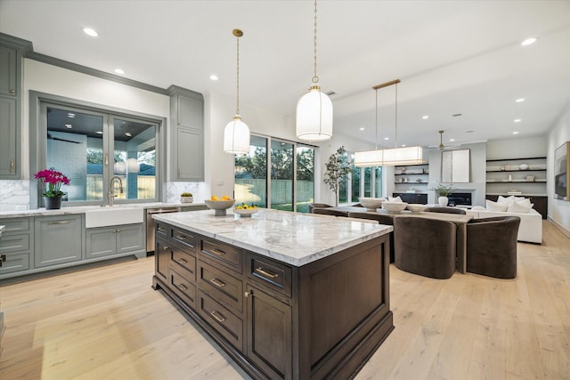 kitchen with a sink, stainless steel dishwasher, light wood finished floors, decorative backsplash, and light stone countertops