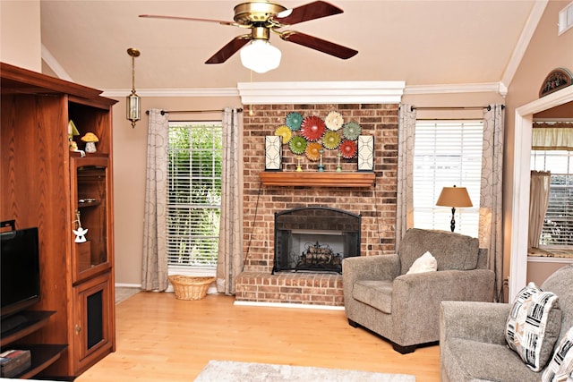 living room featuring a fireplace, light wood-type flooring, crown molding, and a ceiling fan