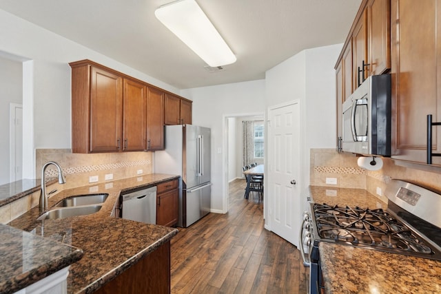 kitchen featuring dark stone countertops, a sink, stainless steel appliances, dark wood-type flooring, and brown cabinets