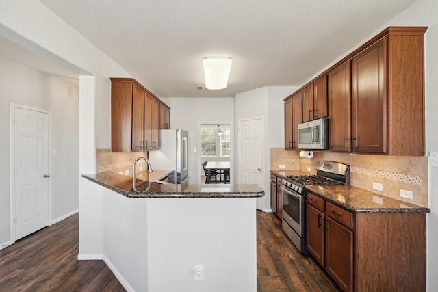 kitchen with tasteful backsplash, dark stone counters, appliances with stainless steel finishes, a peninsula, and dark wood-style floors