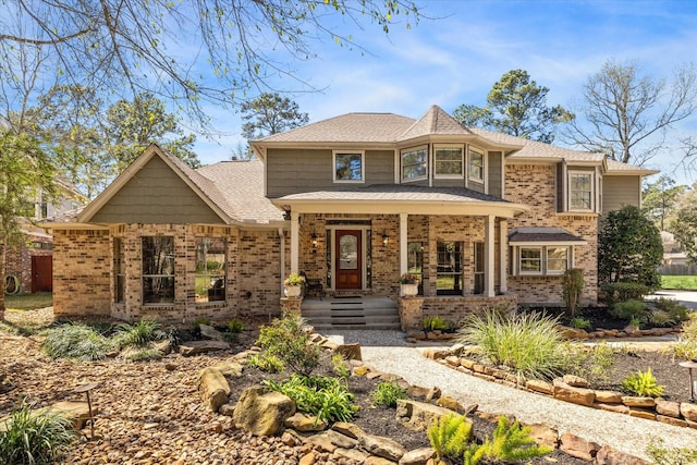 view of front of home with a porch, brick siding, and roof with shingles