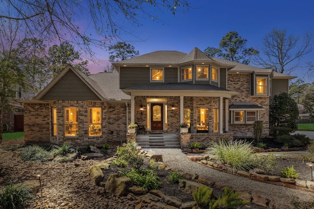 view of front of house with covered porch, brick siding, and a shingled roof