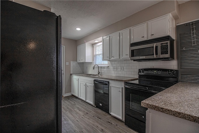 kitchen featuring black appliances, a sink, white cabinetry, light wood finished floors, and decorative backsplash