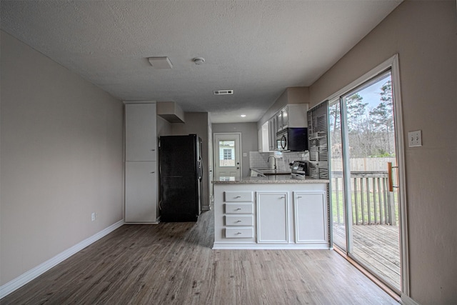 kitchen featuring visible vents, a sink, stainless steel microwave, wood finished floors, and freestanding refrigerator