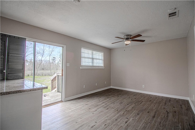 empty room with visible vents, baseboards, wood finished floors, a textured ceiling, and a ceiling fan