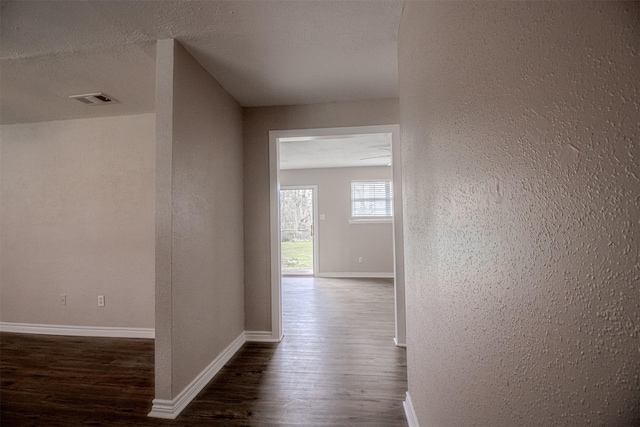 hall featuring visible vents, a textured ceiling, dark wood finished floors, baseboards, and a textured wall