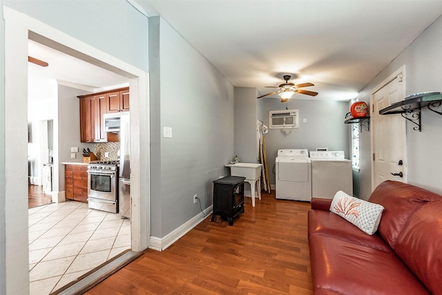 living room featuring an AC wall unit, washing machine and dryer, light wood finished floors, ceiling fan, and a wood stove