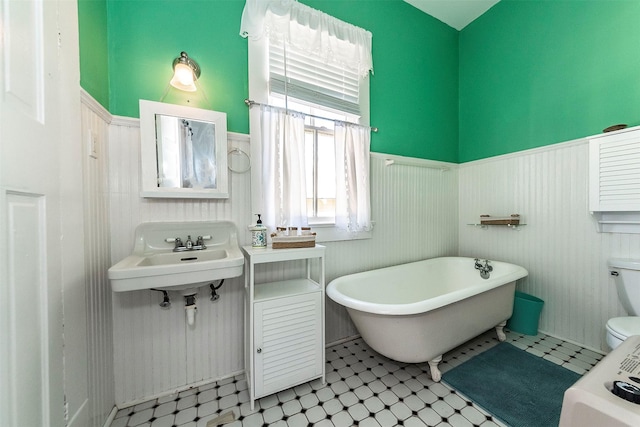 bathroom with a freestanding tub, a sink, wainscoting, tile patterned floors, and toilet