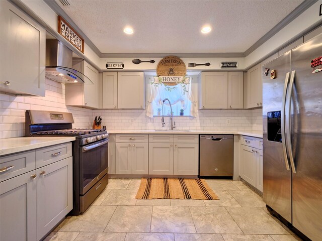 kitchen with gray cabinets, a sink, wall chimney range hood, stainless steel appliances, and light countertops