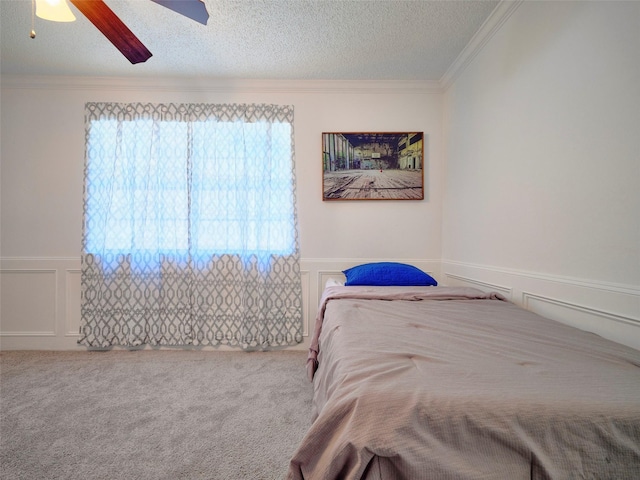 bedroom with a textured ceiling, ceiling fan, ornamental molding, wainscoting, and carpet flooring