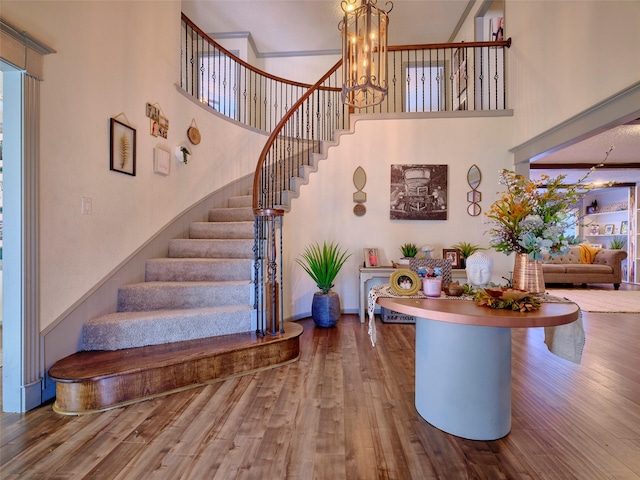 staircase with baseboards, wood finished floors, a chandelier, and a towering ceiling