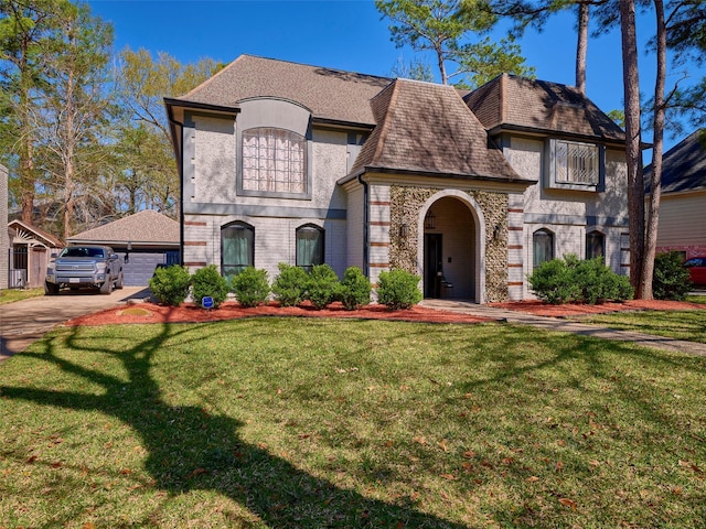 french country style house with stucco siding, a front lawn, a shingled roof, a garage, and brick siding